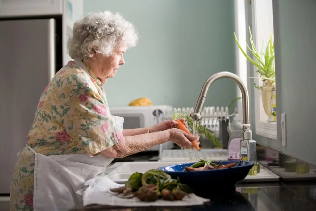 A senior citizen washing vegetables