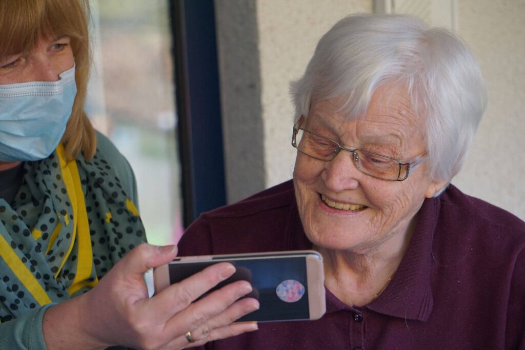 A caregiver shows an elderly woman her cell phone